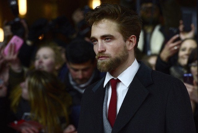 Robert Pattinson poses for cameras while fans group behind him