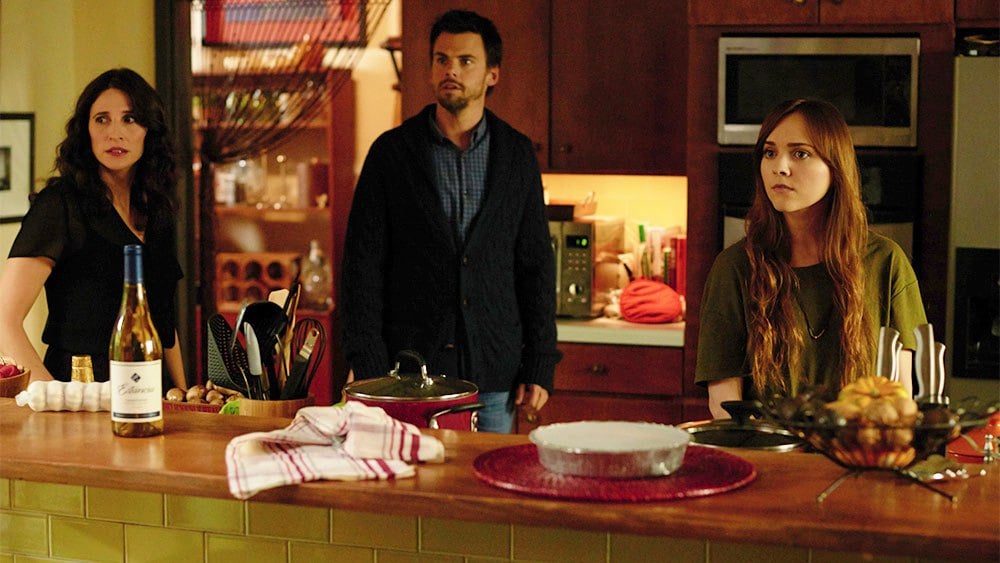 Two adults and a young woman stand behind a counter in a kitchen in Casual