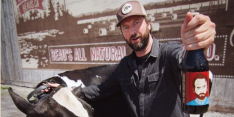 Tom Green tenant une bouteille de la bière Tom Green à côté d'une vache