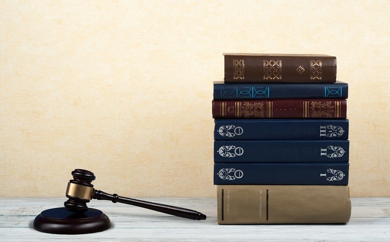 Concetto di legge libro aperto con martelletto di legno dei giudici sul tavolo in un'aula di tribunale o ufficio delle forze dell'ordine, sfondo blu.