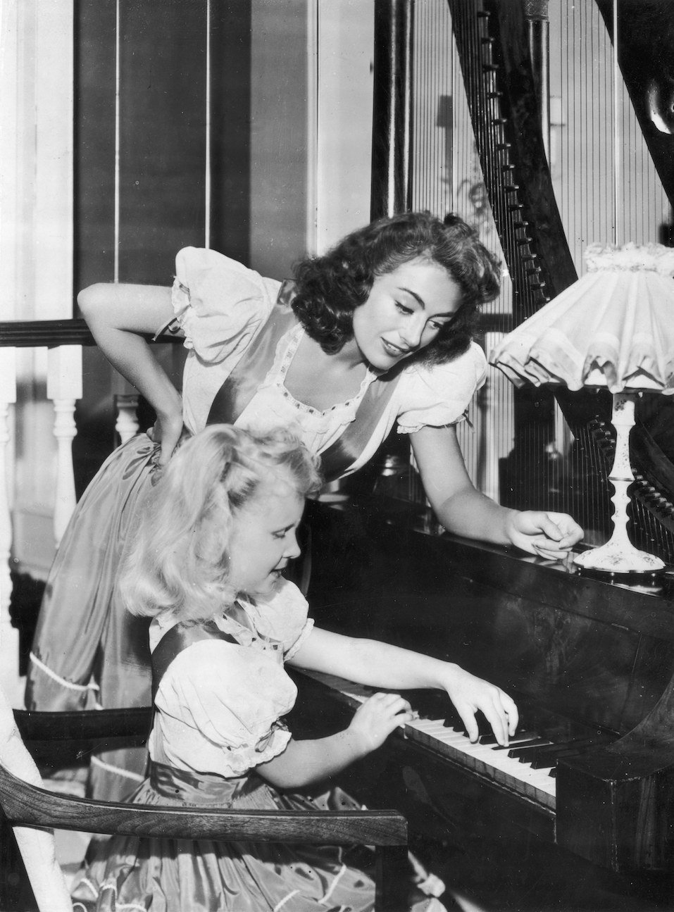 Hollywood actress Joan Crawford supervises her adoptive daughter Christina's piano practice