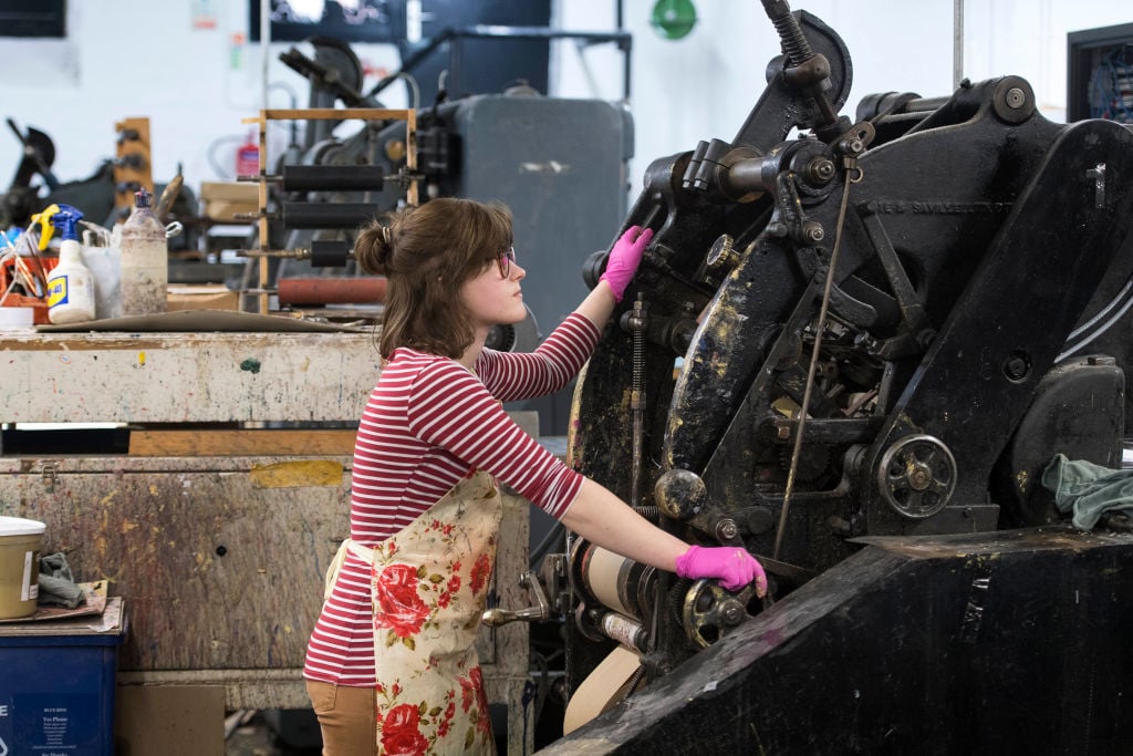 Woman uses the die stamping press at the workshop of Barnard and Westwood 