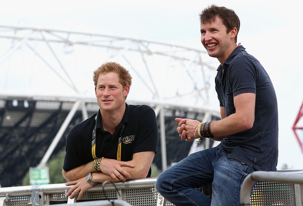 Prince Harry and James Blunt outside a stadium, smiling