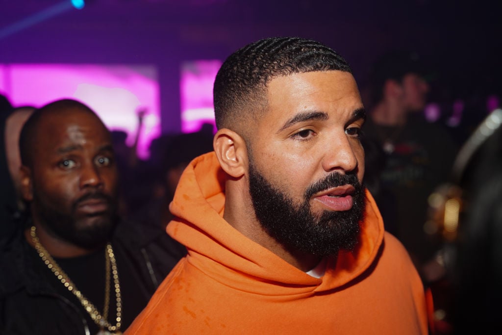 Drake in an orange sweatshirt looking off camera