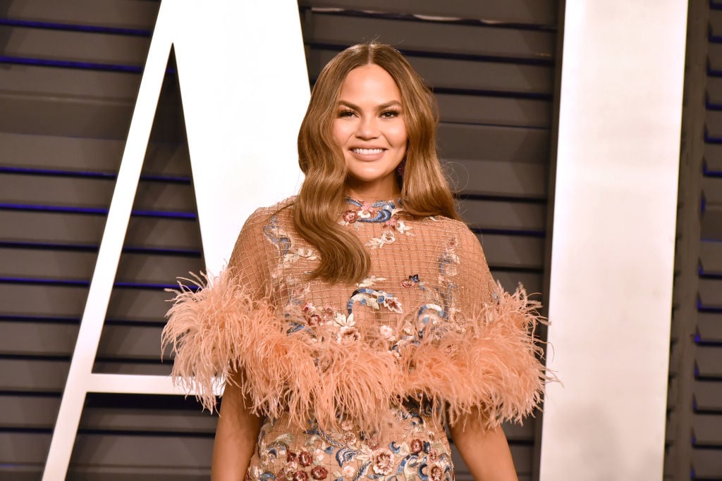 Chrissy Teigen smiling in a pink dress