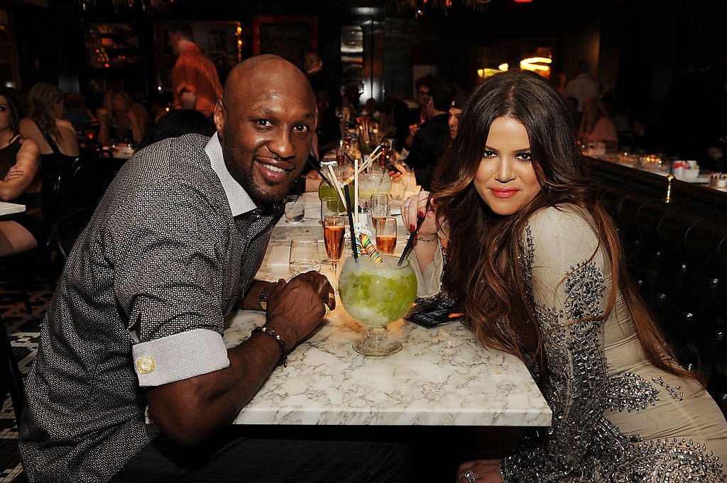 Lamar Odom and Khloé Kardashian sitting on opposite sides of a dinner table, smiling at the camera