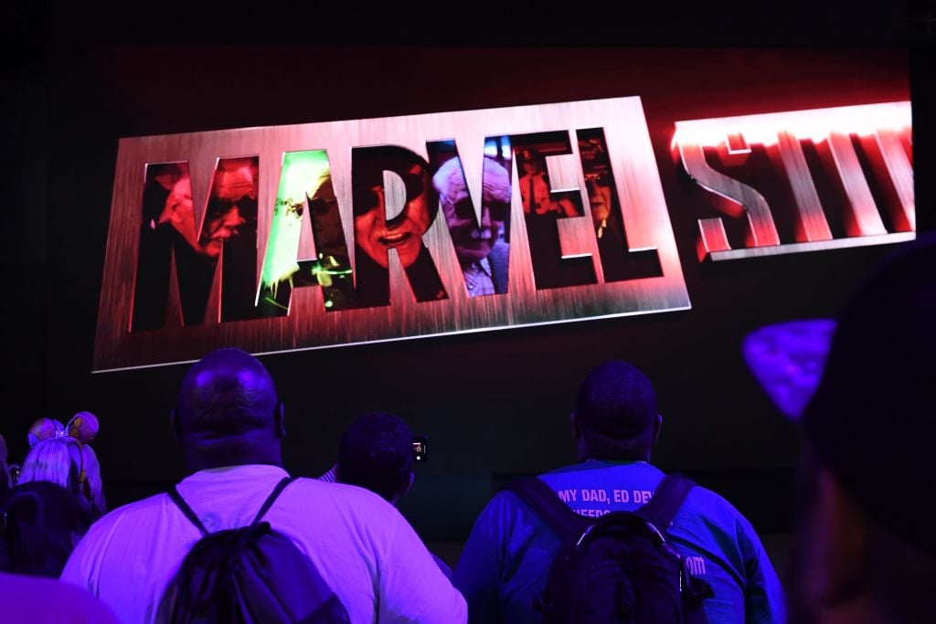 Marvel Studios logo lit up with people in backpacks looking up at the logo