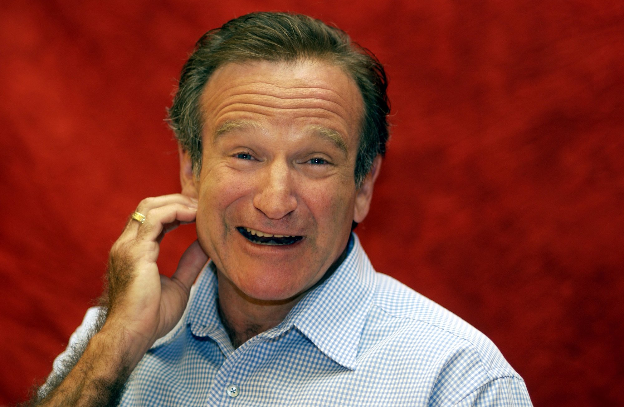 Robin Williams smiling in front of a red background
