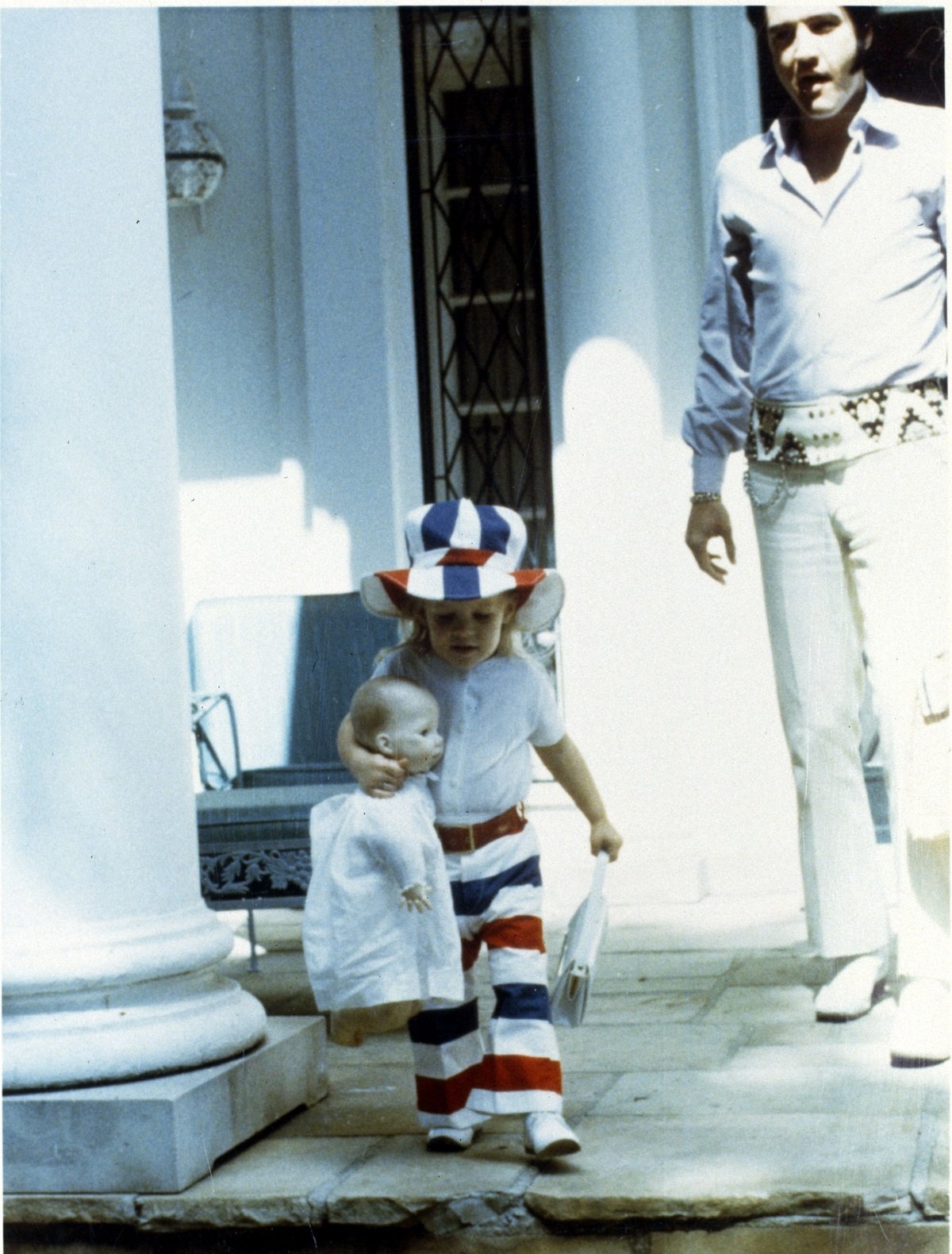 Lisa Marie Presley as a child with a doll with Elvis Presley in the background in a candid shot