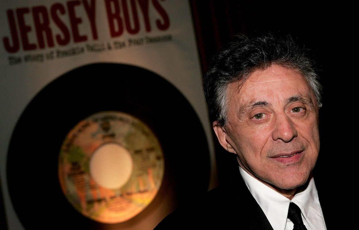 Frankie Valli looks at the camera with a 'Jersey Boys' poster behind him, 2005