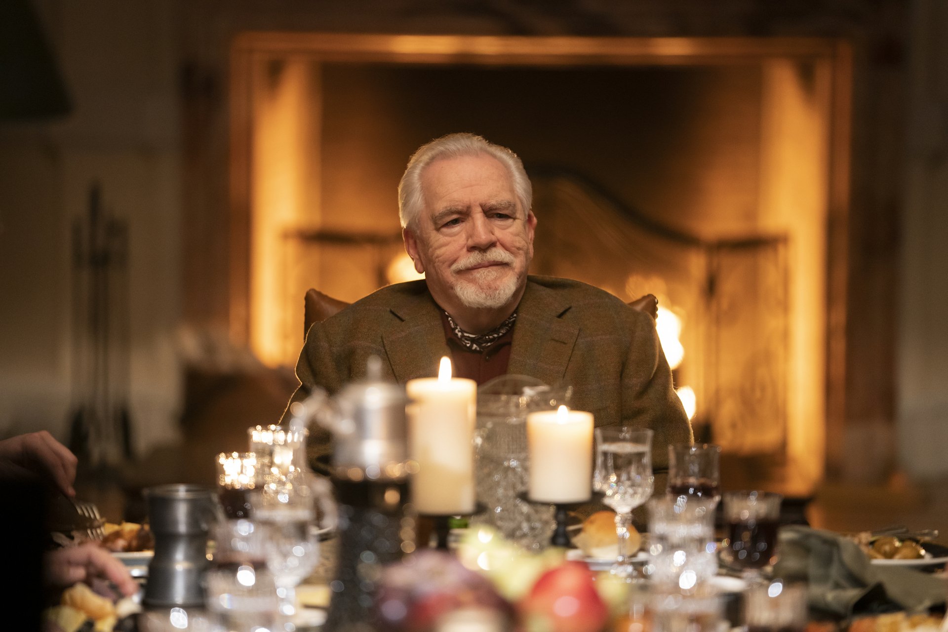 Brian Cox sits at a table with candles and crystal glasses in 'Succession.'