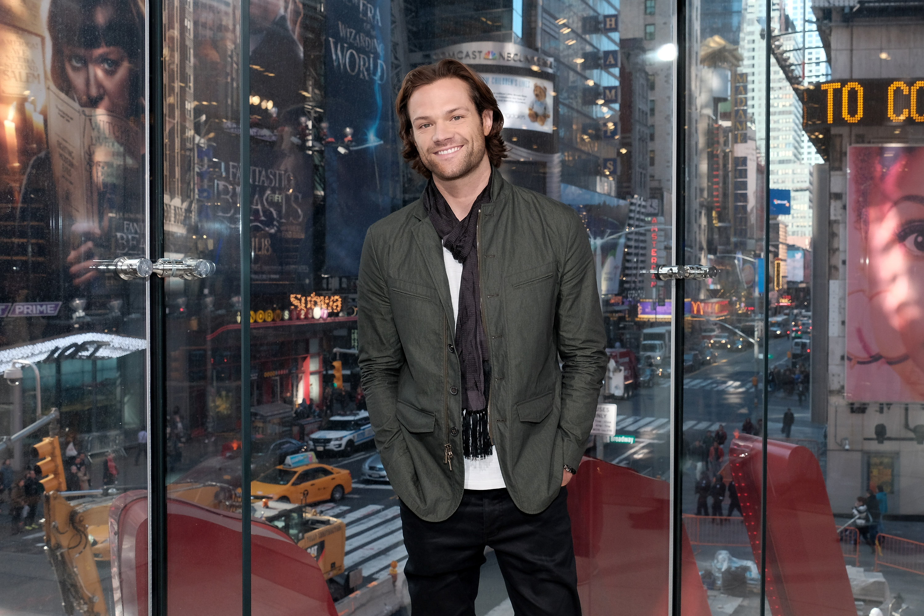 Jared Padalecki smiling in front of Times Square window