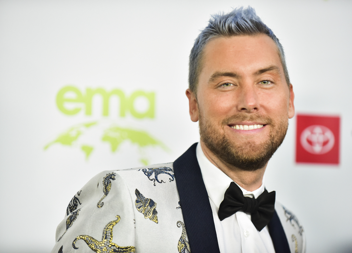 Lance Bass, wearing a tuxedo, faces the camera and smiles.