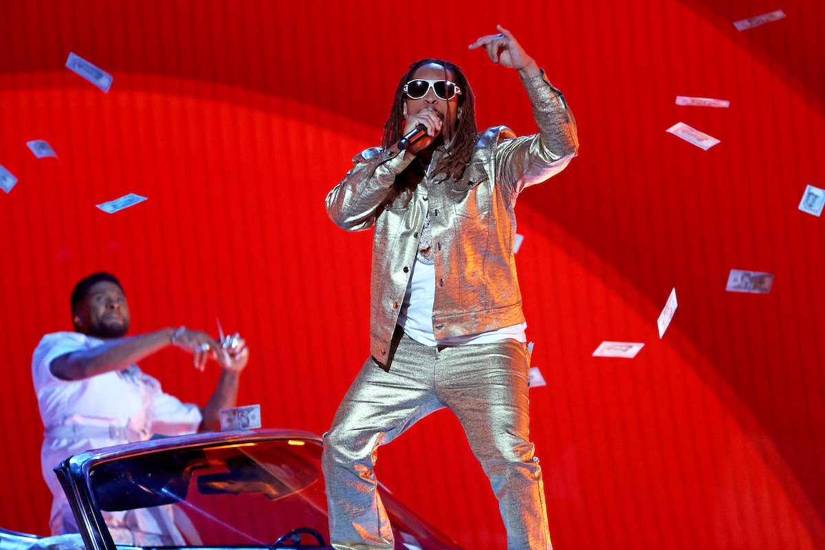 Lil jon performs on stage in a white outfit with money falling around him.