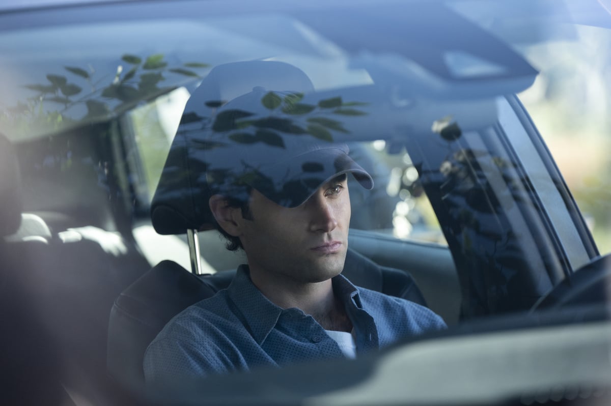 Joe sits in his car wearing a blue baseball cap and a button-down shirt.