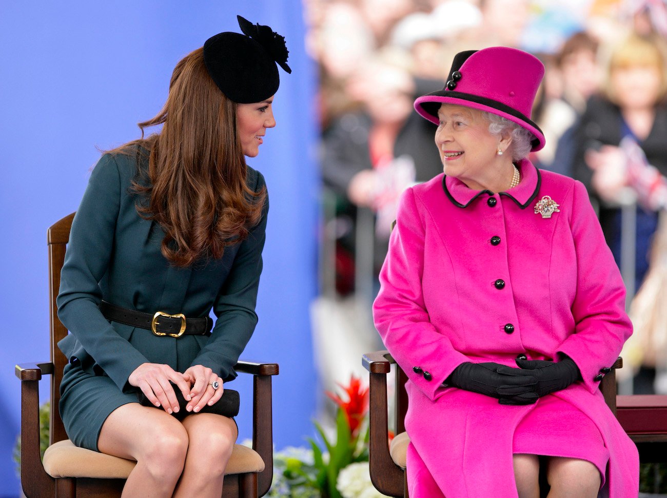 Queen Elizabeth II smiles wearing a pink suit as Kate Middleton speaks to her