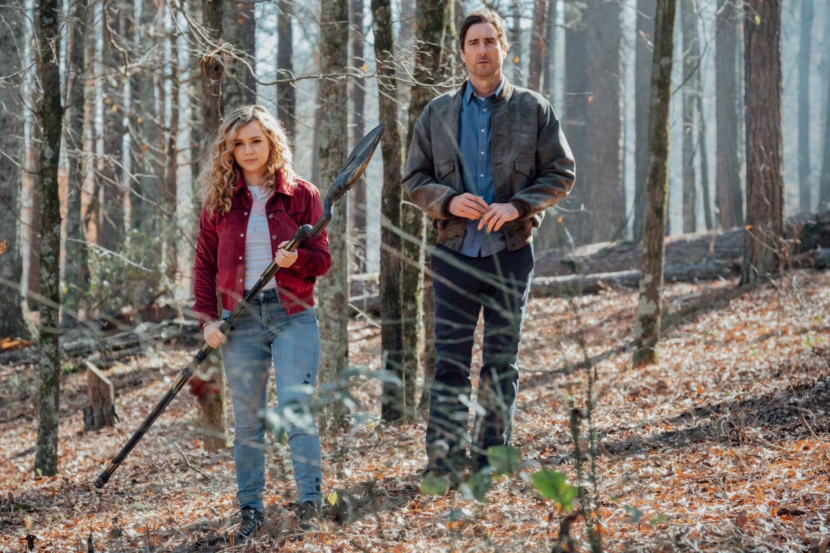 'Stargirl' Season 2 finale actors Brec Bassinger and Luke Wilson in character as Courtney Whitmore and Pat Dugan. Bassinger wields the Cosmic Staff and wears a red jacket over a white shirt and jeans. Wilson wears a brown jacket over a blue button-up shirt and jeans.