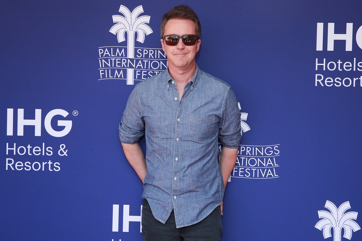 Edward Norton wearing a button up shirt and sunglasses while smirking