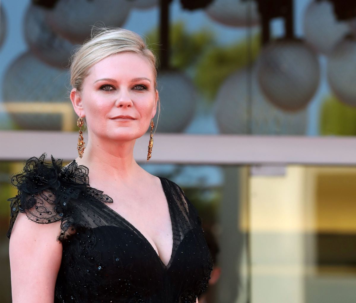 Kirsten Dunst in a black dress, with her hair up, and smiling slightly