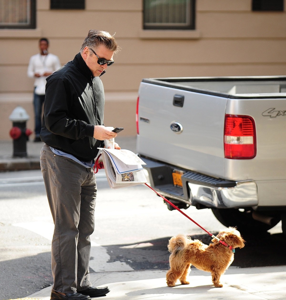 Alec Baldwin looking at his cell phone while walking a dog