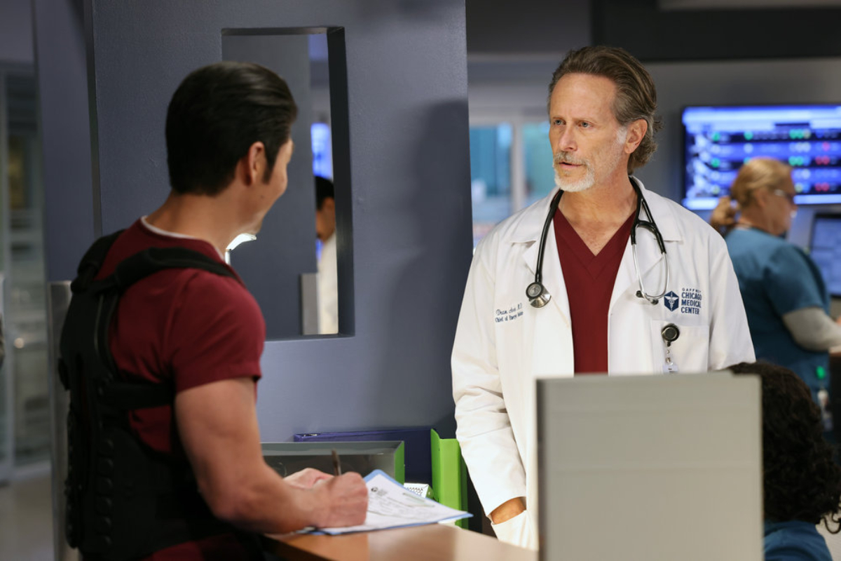 Brian Tee as Ethan Choi and Steven Weber as Dr. Dean Archer in Chicago Med Season 7. Archer faces Choi while Choi looks up from writing something.