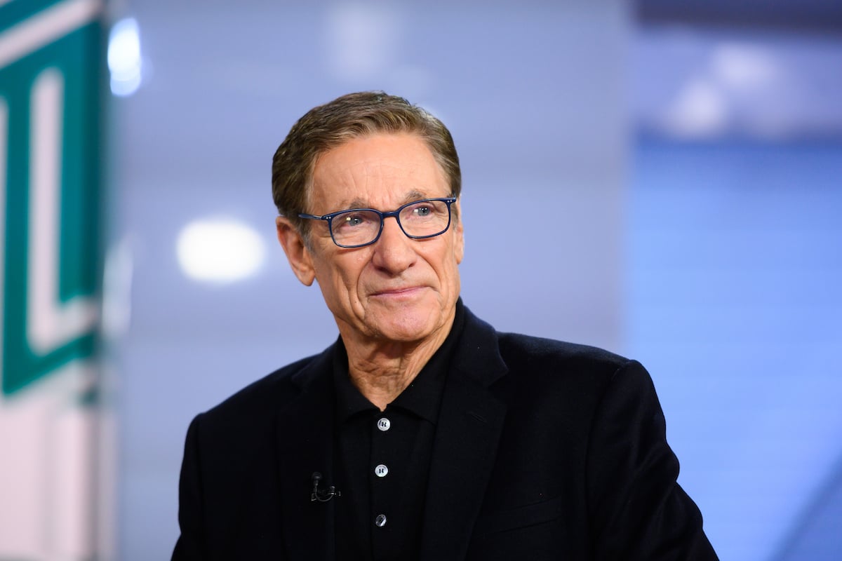 Maury Povich in black suit and blue glasses.