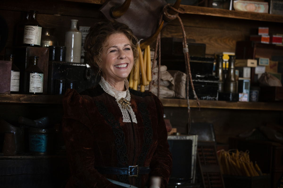 Rita Wilson as Carolyn of the Paramount+ original series 1883. Carolyn stands in the shop and smiles warmly.