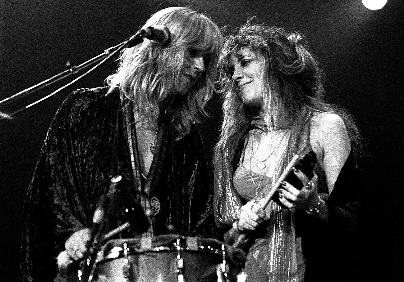 Christine McVie and Stevie Nicks stand staring at each other in front of a drum and microphone.