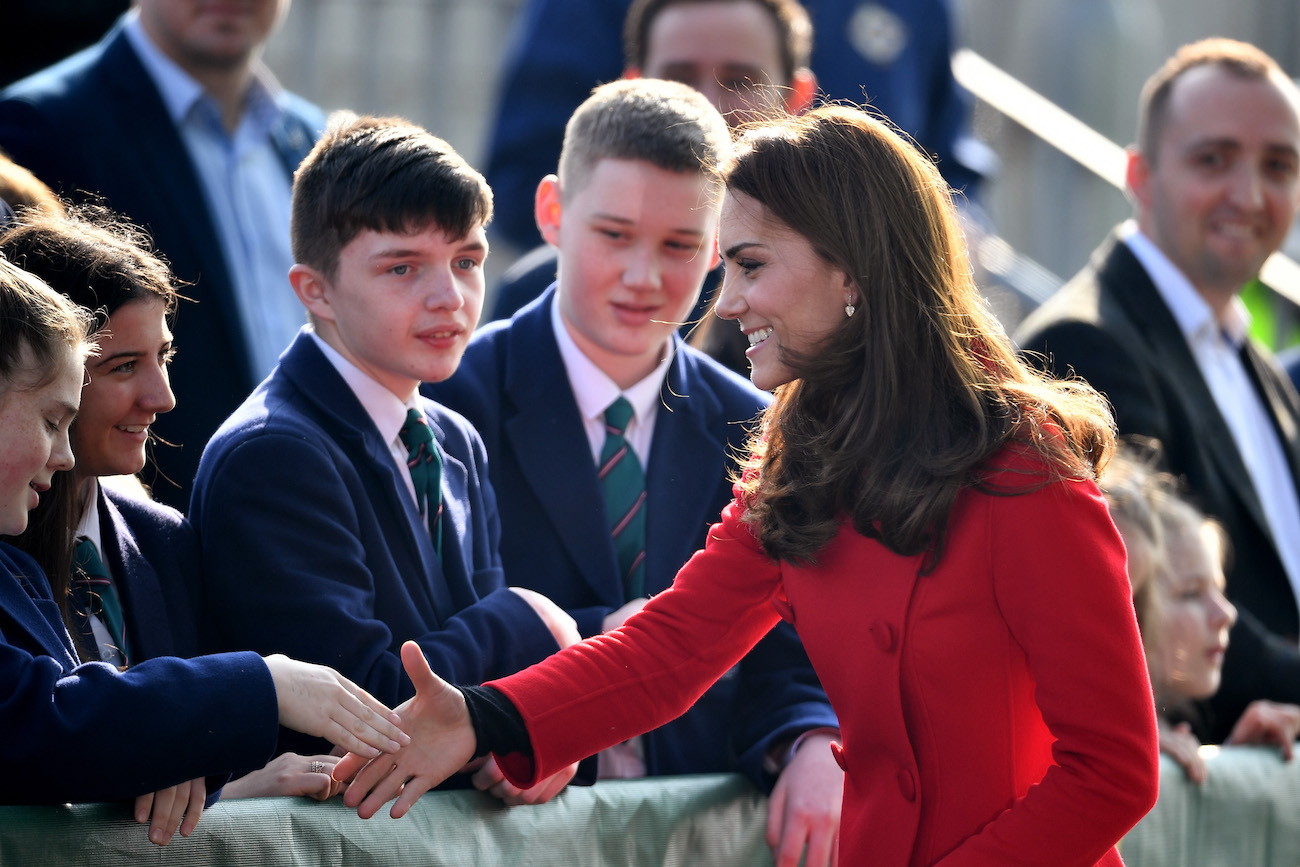 Kate Middleton smiles as she puts her hand out to shake the hands of children