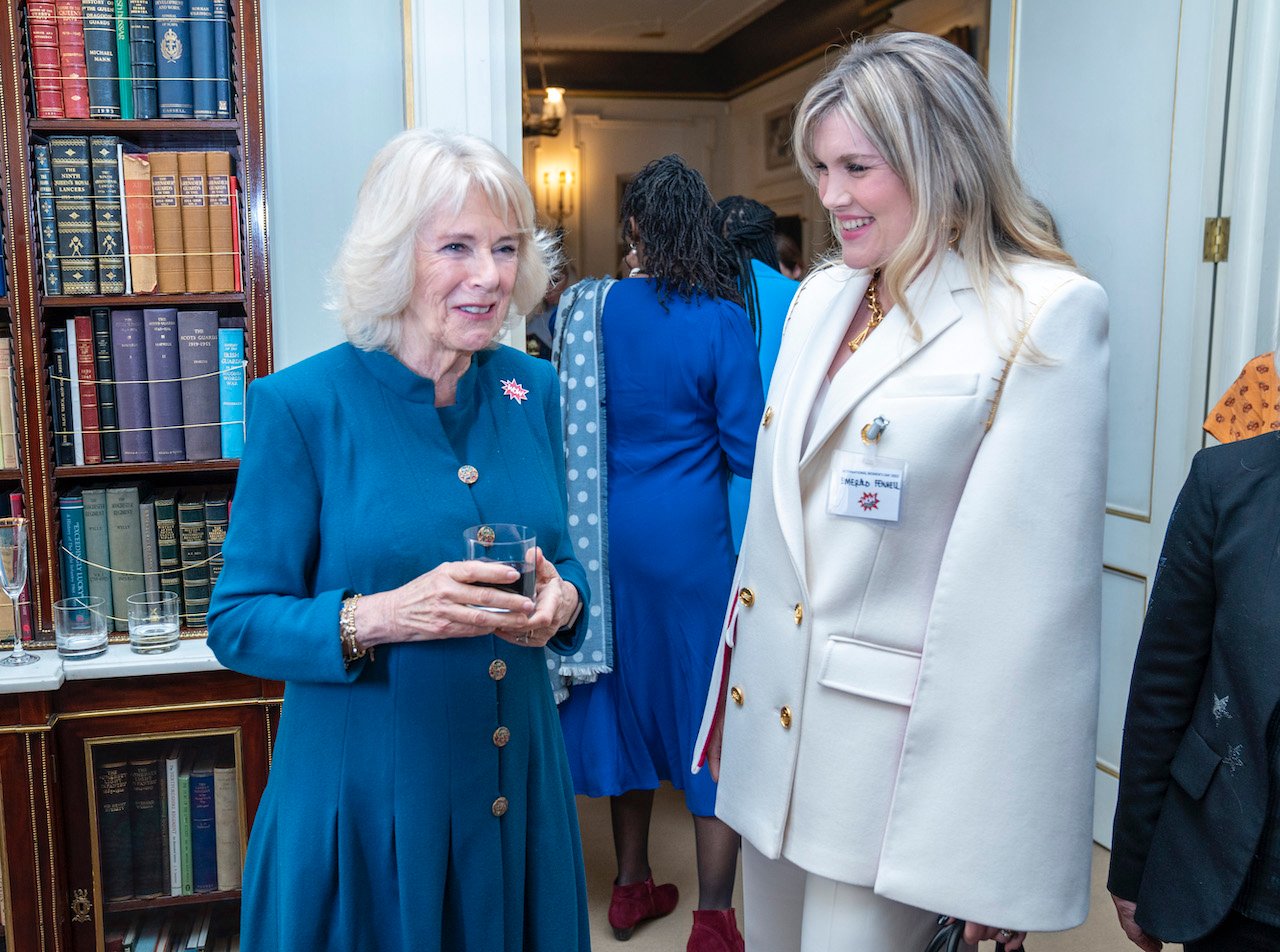 The Duchess of Cornwall Camilla Parker Bowles smiles wearing a blue dress with Emerald Fennell of 'The Crown', who wears a white jacket.