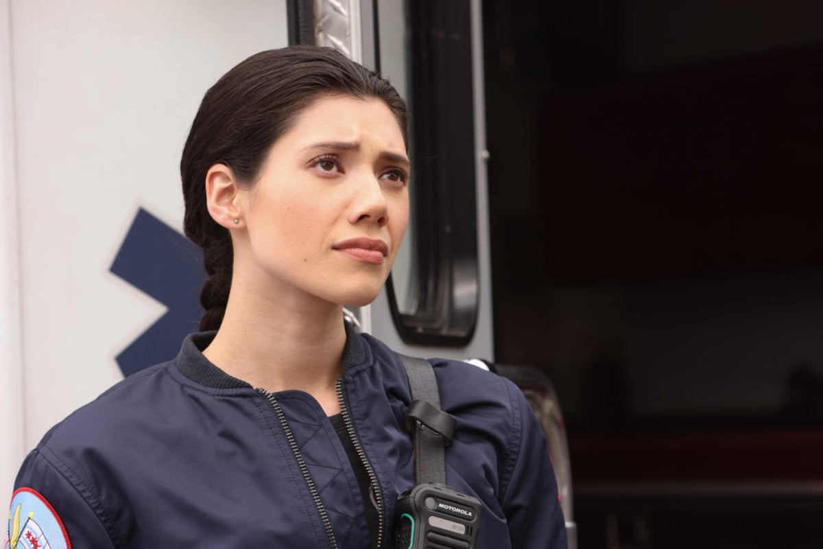 Violet Mikami, a series regular in Chicago Fire Season 10, wearing a blue jacket and standing outside an ambulance. 