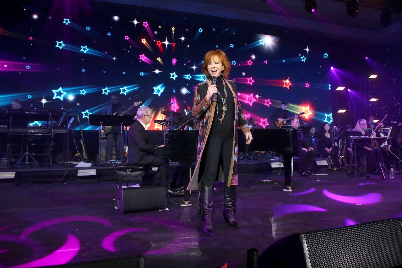 Reba McEntire sings and David Foster plays the piano in front of a colorful background