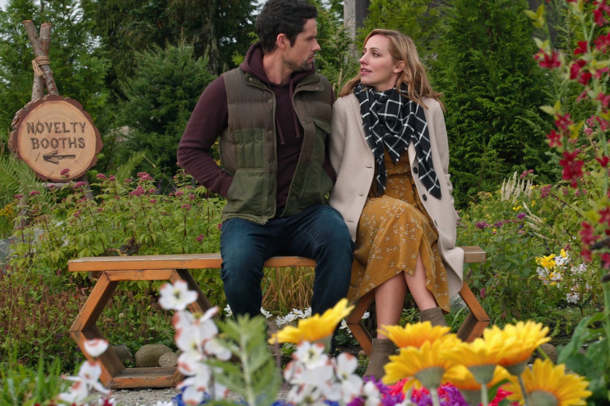 Ben Hollingsworth as Brady and Zibby Allen as Brie sitting on a wooden bench in a colorful garden on 'Virgin River'