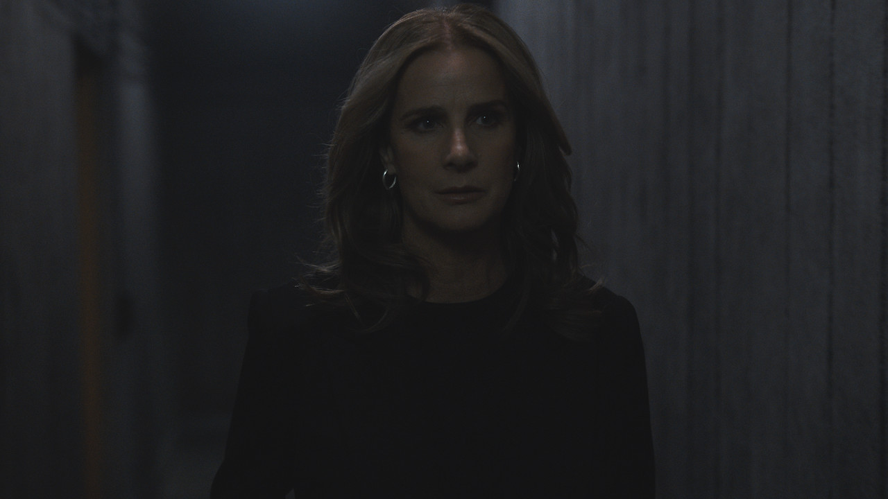 Rachel Griffiths as Gretchen Klein in 'The Wilds' stands in a dark hallway.