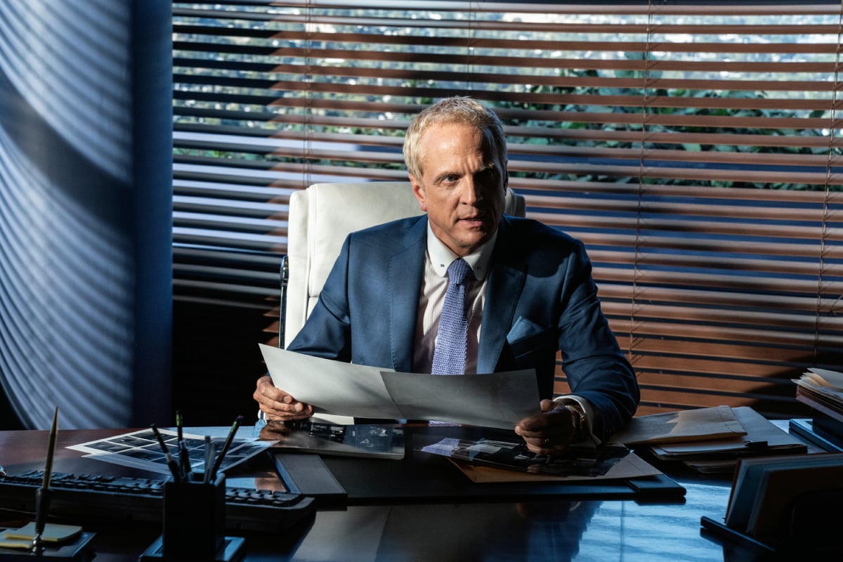 Patrick Fabian as Howard Hamlin in Better Call Saul Season 6. Howard sits at his desk holding papers and wears a blue suit. 