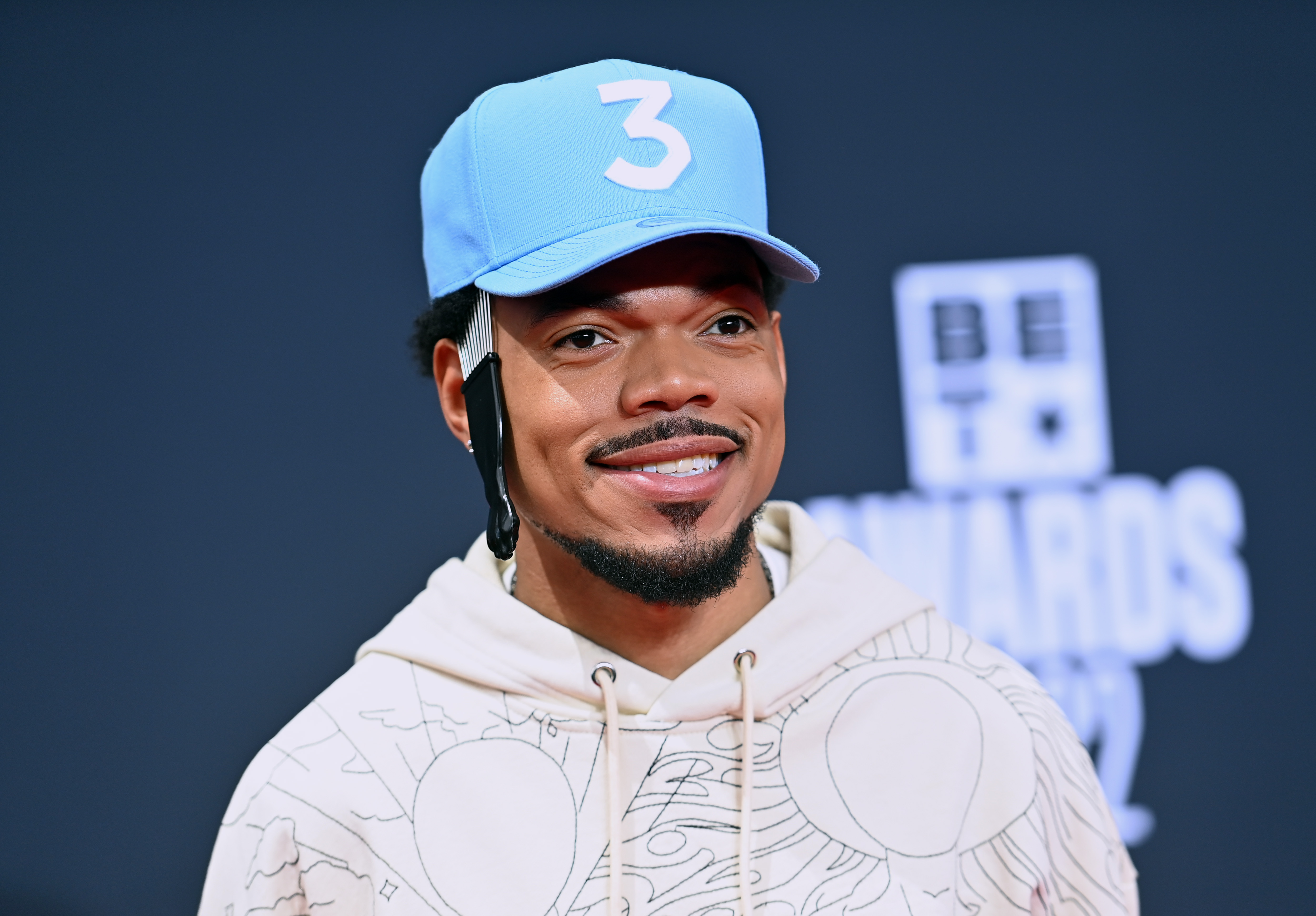 Famous musician Chance the Rapper wearing a blue hat smiling for photographers.