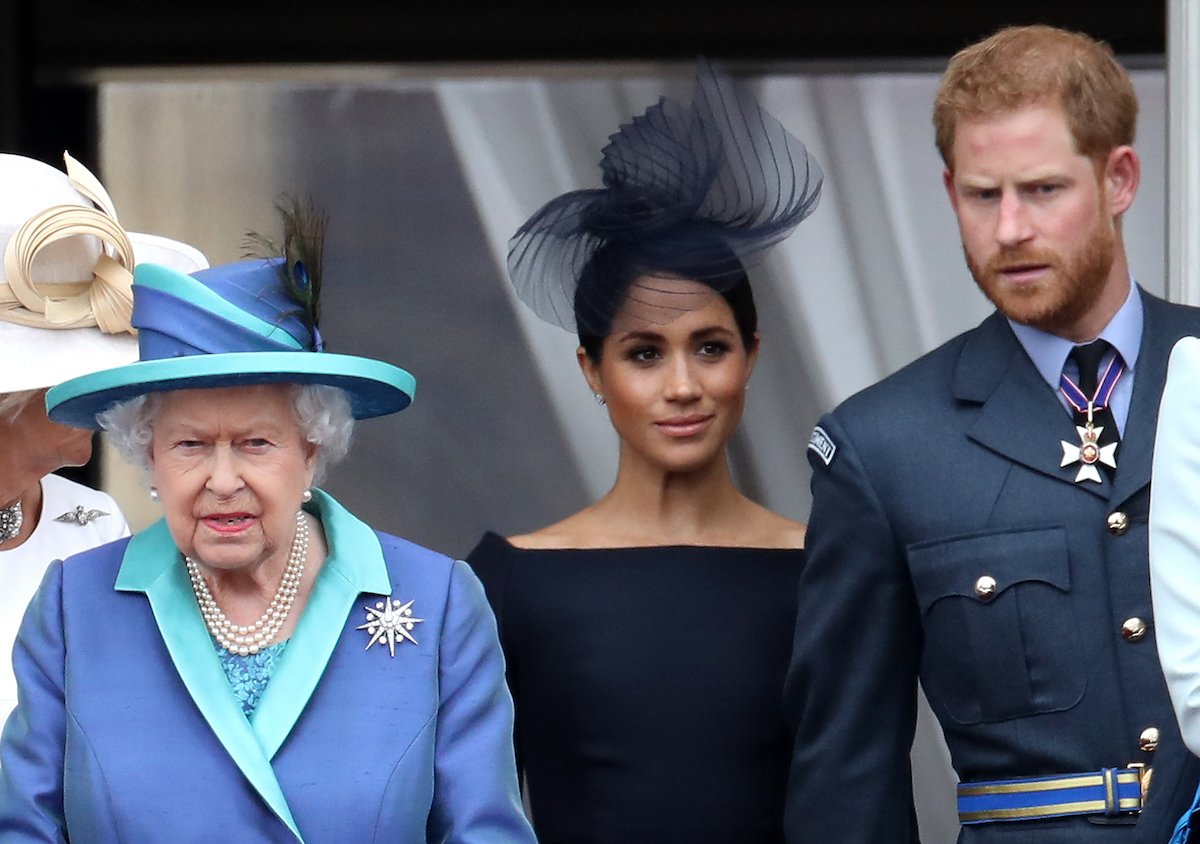 Queen Elizabeth, who a royal expert says had another reason for meeting Lilibet only briefly, stands next to Meghan Markle and Prince Harry