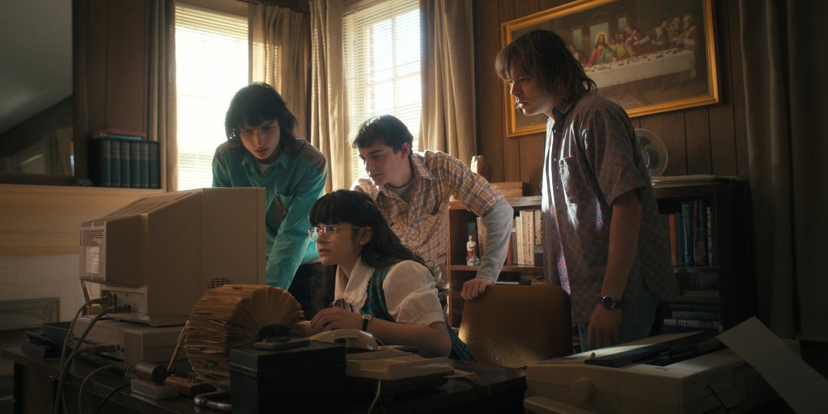 Mike, Will, and Jonathan visit Suzie in Stranger Things Season 4. Suzie types on the computer while the boys stare at the screen. 
