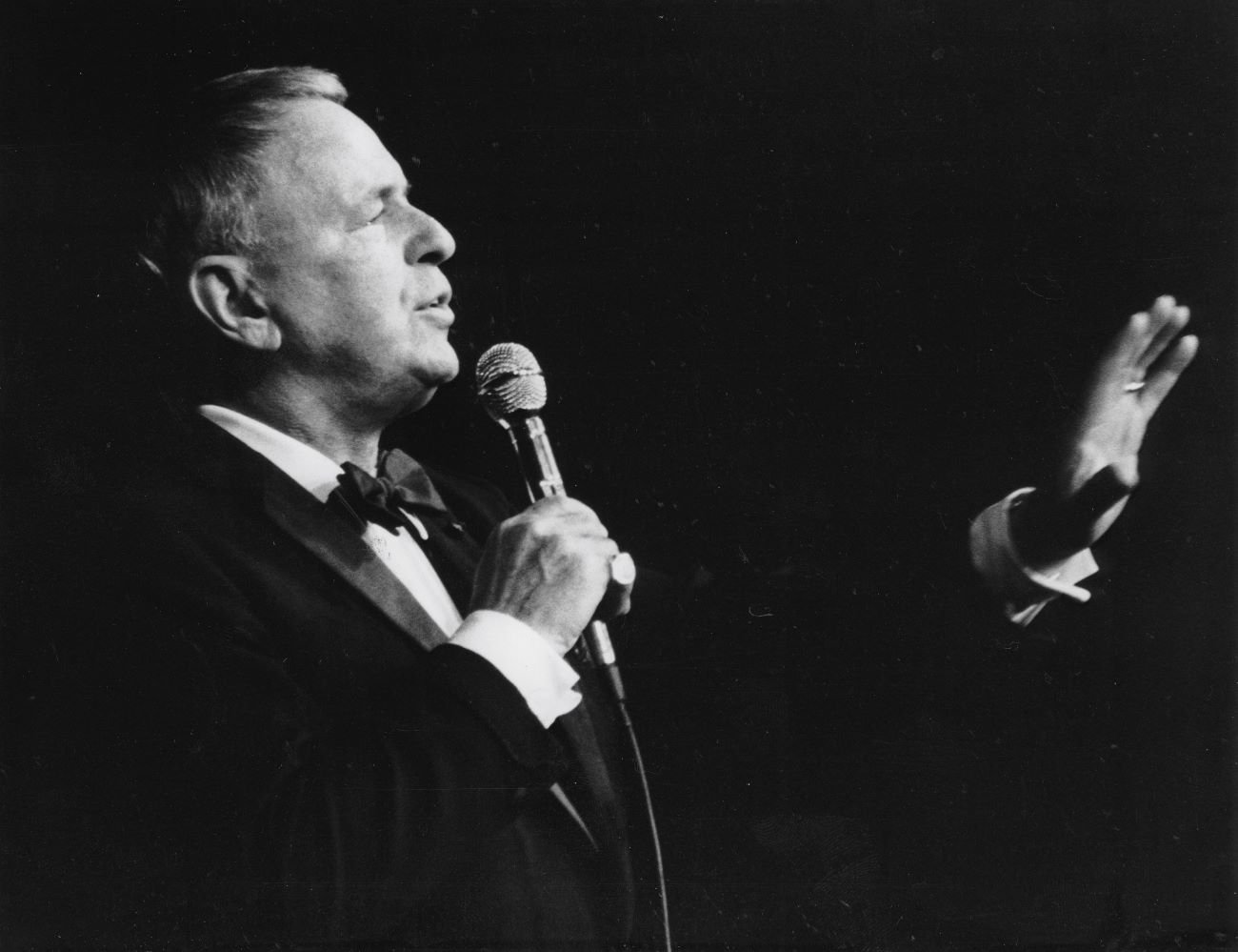 A black and white photo of Frank Sinatra holding a microphone and singing.