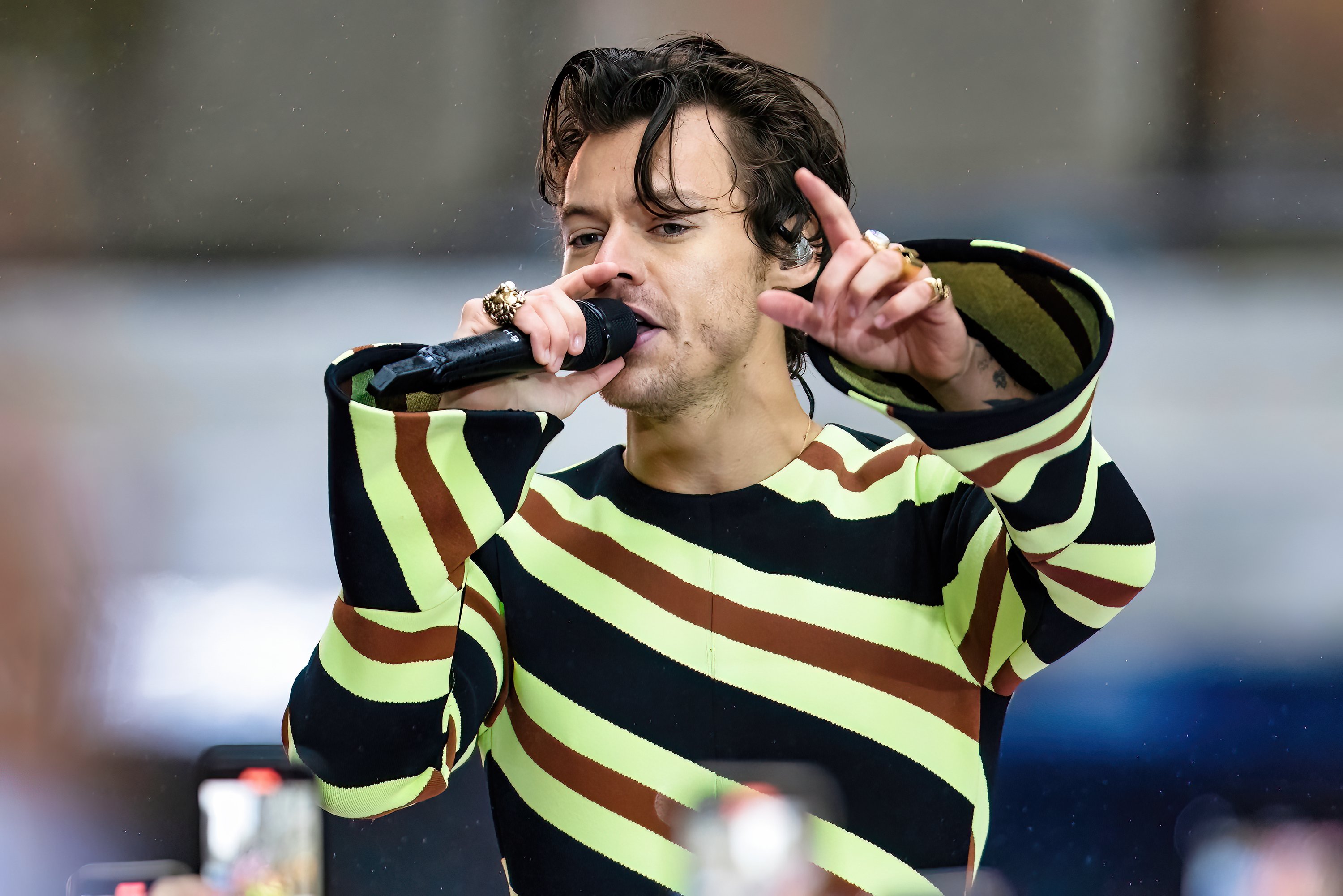 Harry Styles, who made his MCU debut as Eros in 'Eternals,' wears a black, brown, and light green striped jumpsuit while singing onstage.