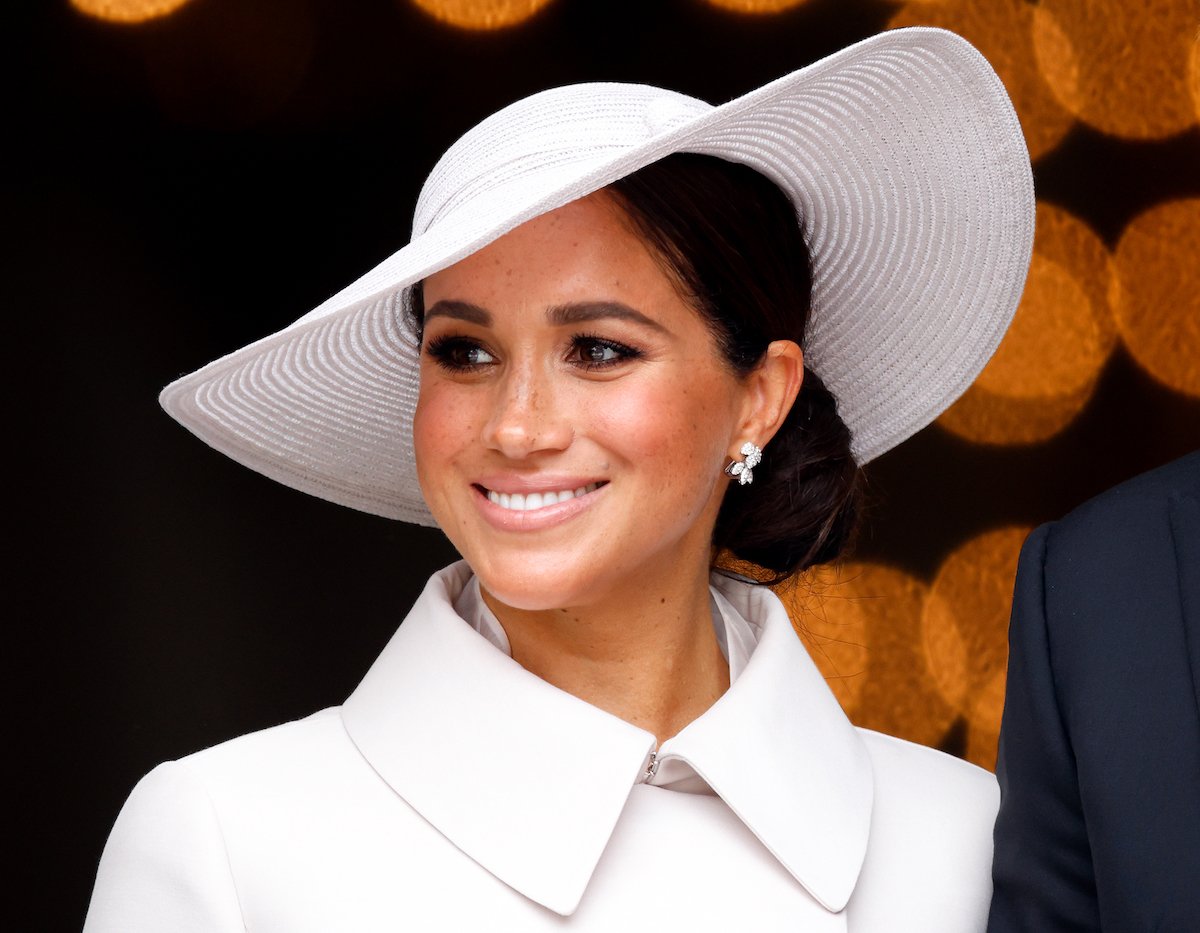 Meghan Markle smiling in a white hat and coat