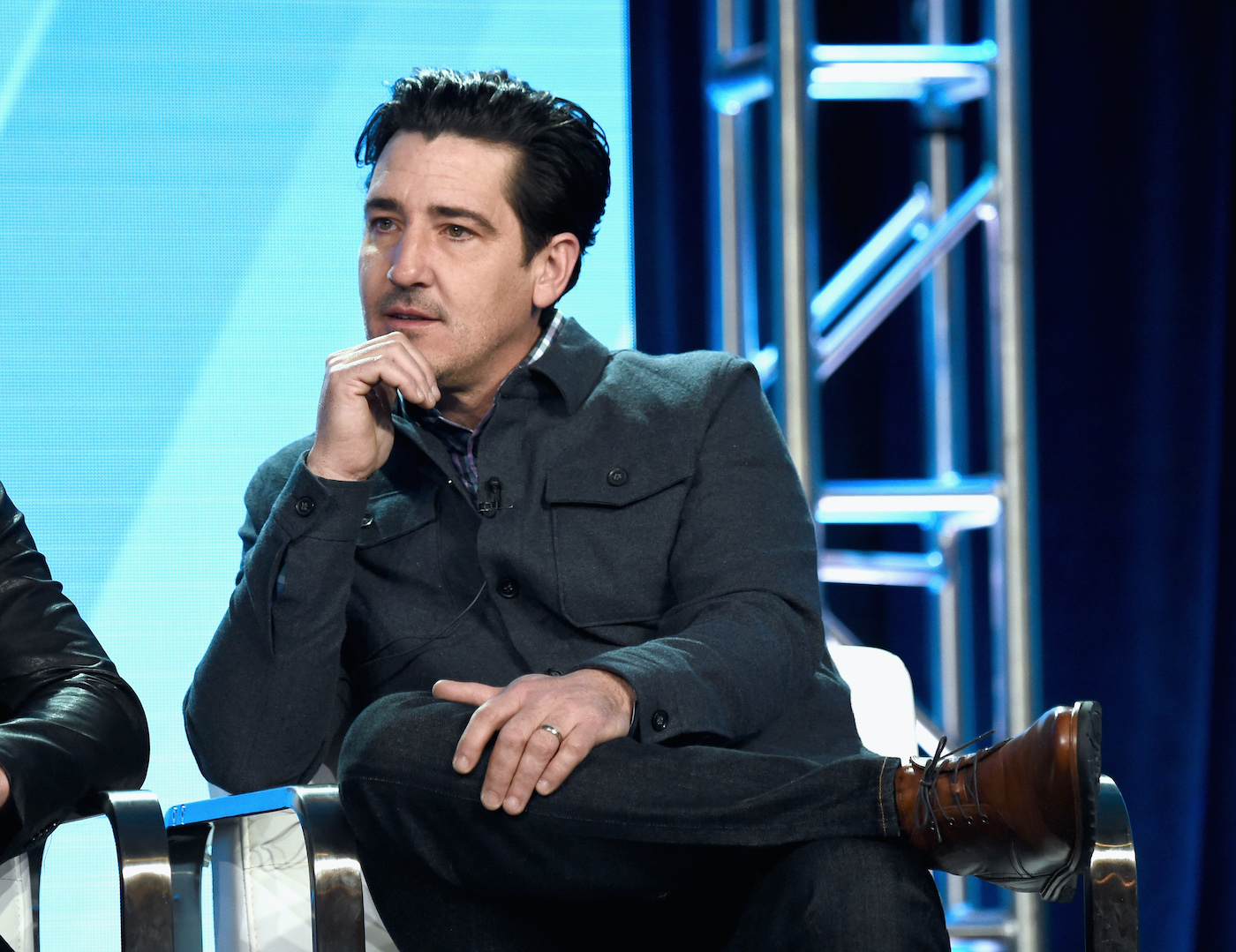 Jonathan Knight from 'Farmhouse Fixer' sits in a chair and rests his chin on his hand 