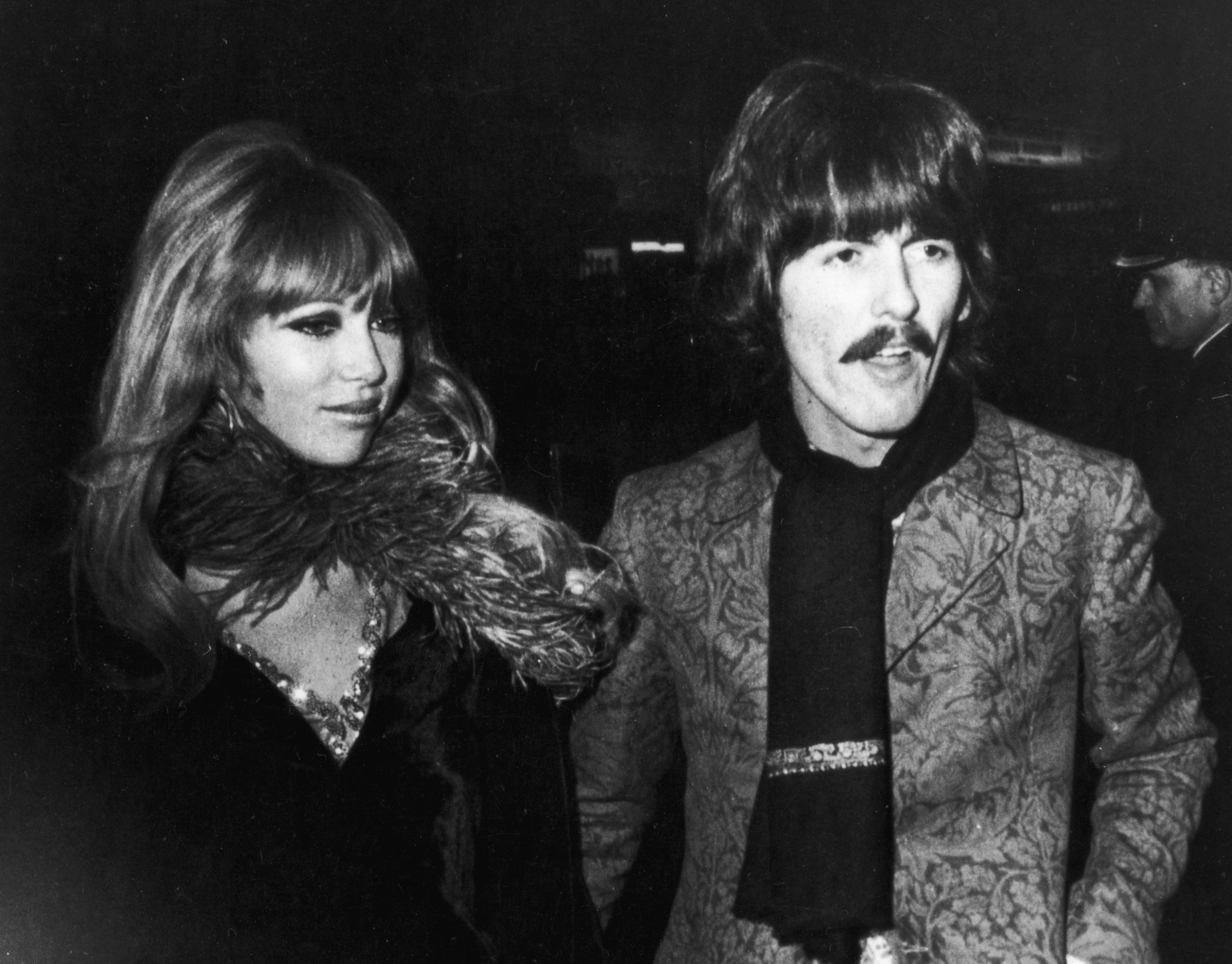 A black and white photo of George Harrison and Pattie Boyd wearing coats and walking outside.