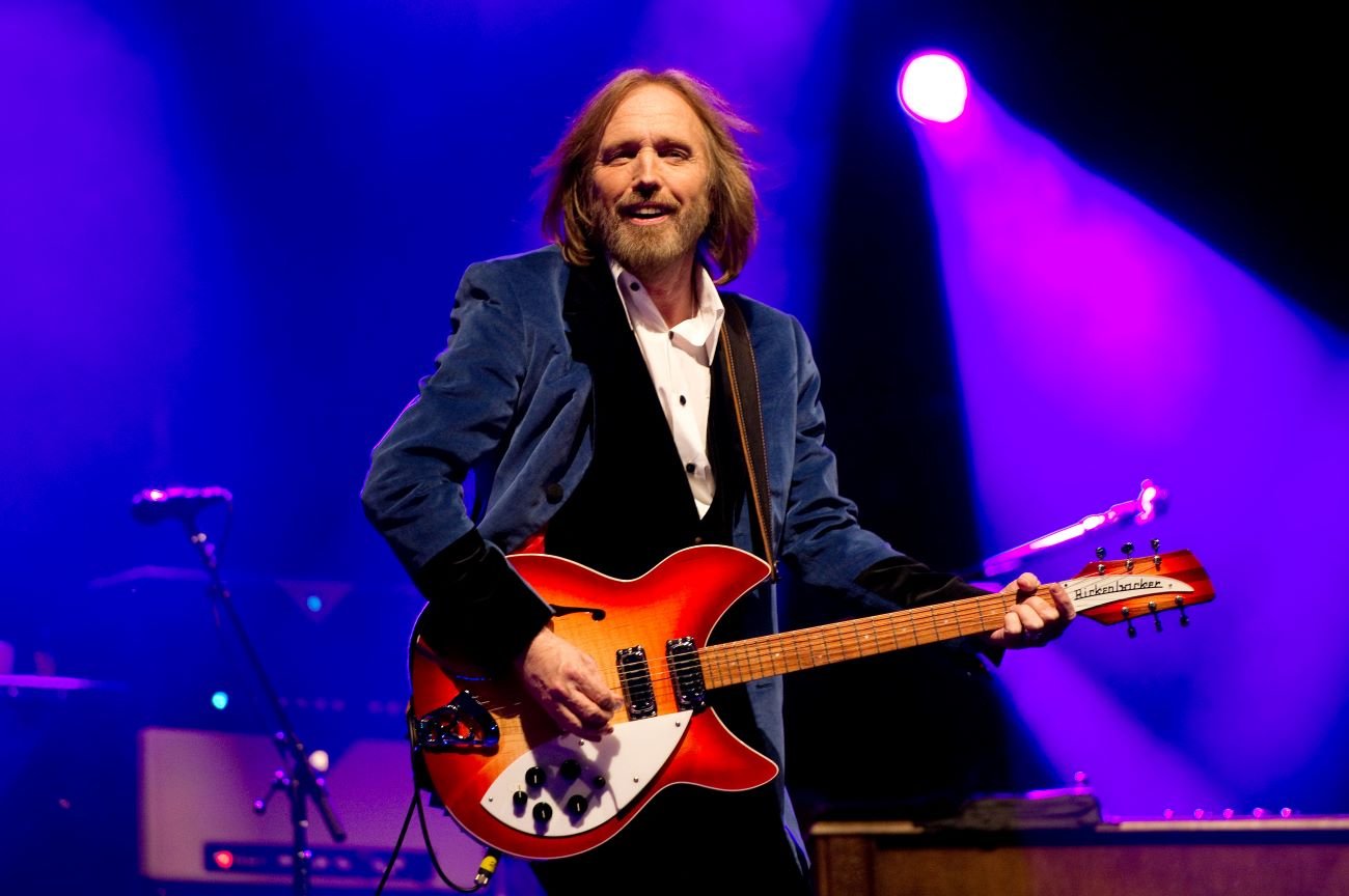 Tom Petty wears a blue jacket and plays a guitar.