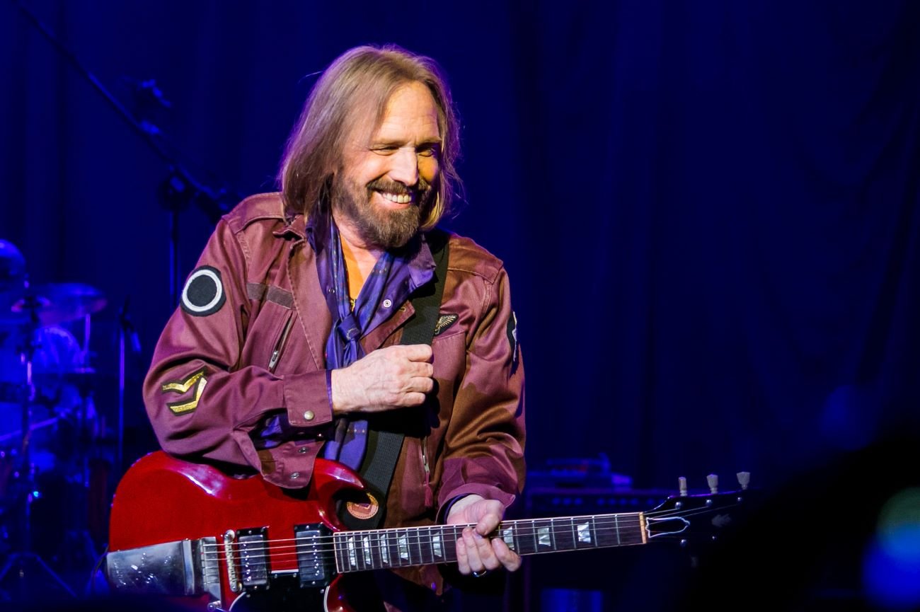 Tom Petty wears a purple jacket and holds a guitar.