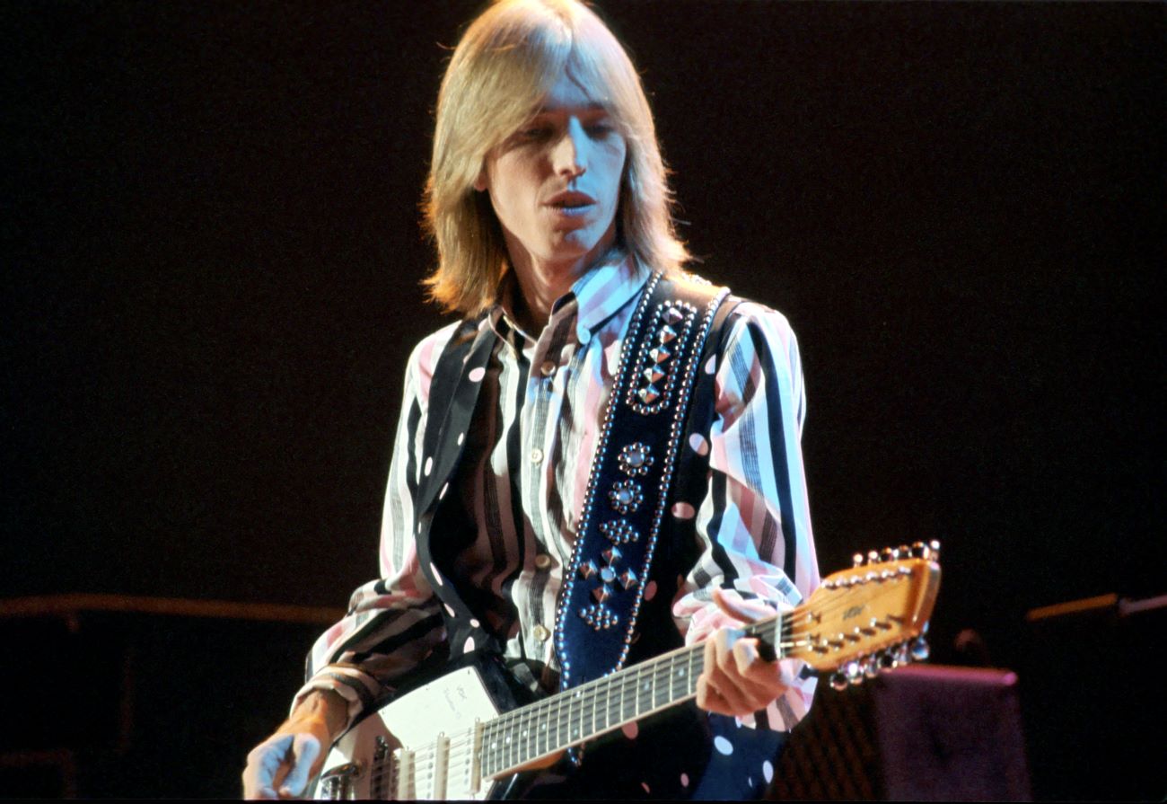 Tom Petty wears a striped shirt and plays the guitar.