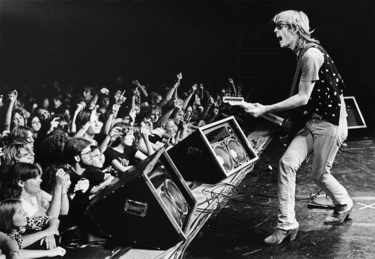 A black and white picture of Tom Petty playing his guitar in front of an audience.