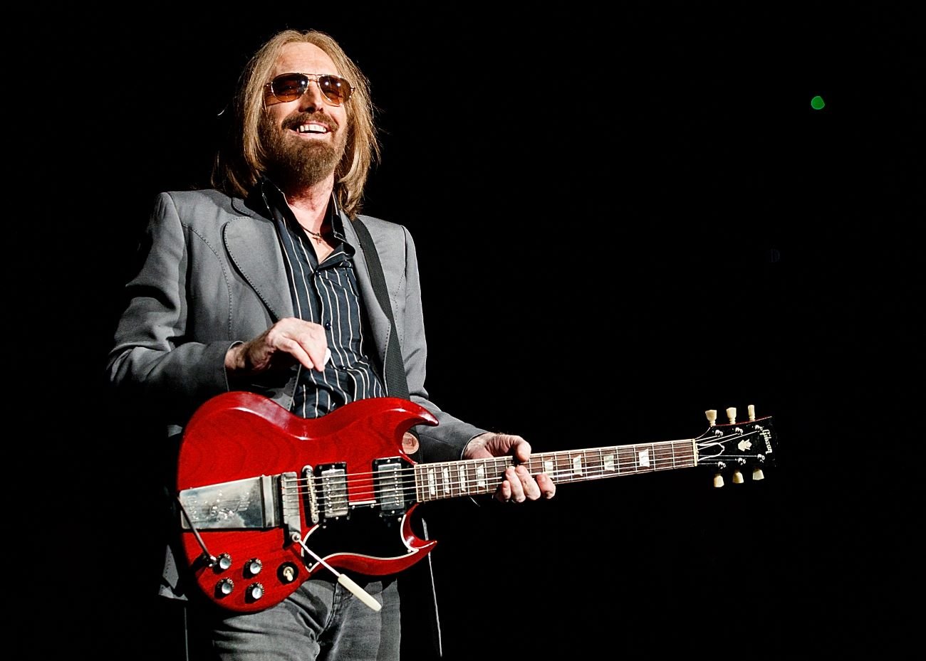 Tom Petty wears sunglasses and holds a guitar.