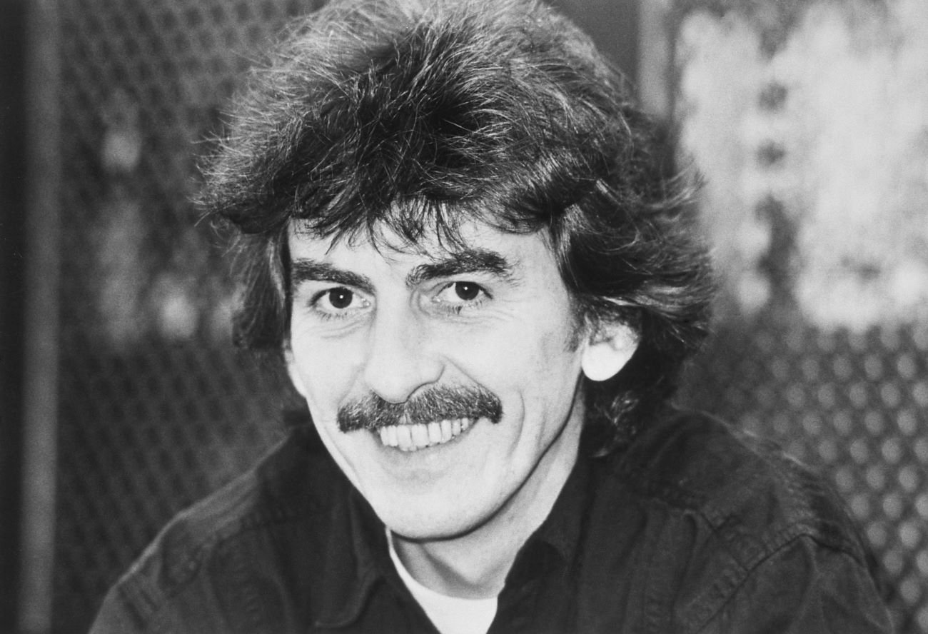 A black and white picture of George Harrison sitting in front of a chain link fence.