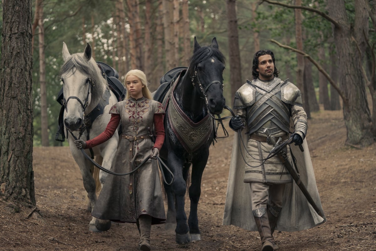 Milly Alcock as Rhaenyra and Fabien Frankel as Criston Cole in House of the Dragon. Rhaenyra and Criston walk with their horses in the woods.